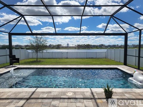 A pool under a glass roof with a fence and a tree in the background.