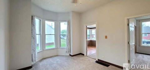 A room with a carpeted floor and a window with a view of a house across the way.