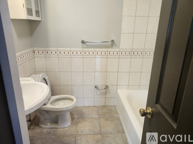 A white toilet sits in a bathroom with a white tiled wall.