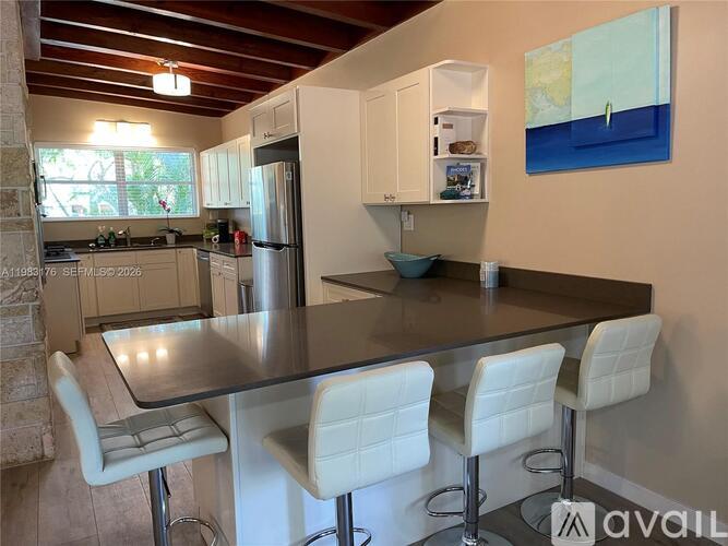 A kitchen with a table and chairs in the foreground and a painting on the wall.