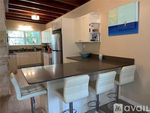 A kitchen with a table and chairs in the foreground and a painting on the wall.