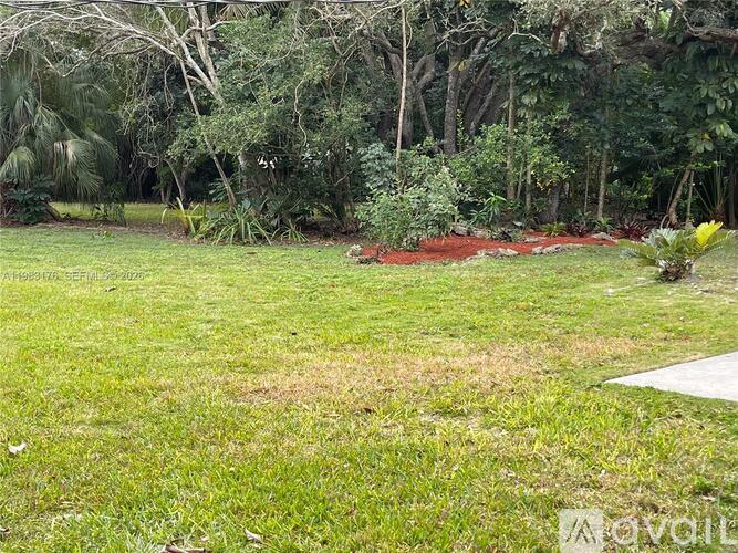 A grassy area with a red patch in the middle and trees in the background.