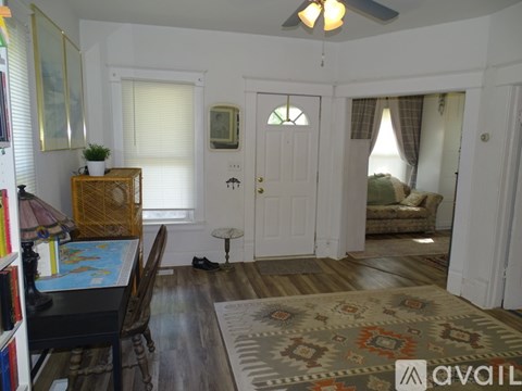 A living room with a rug on the floor and a wooden table with a lamp and books on it.