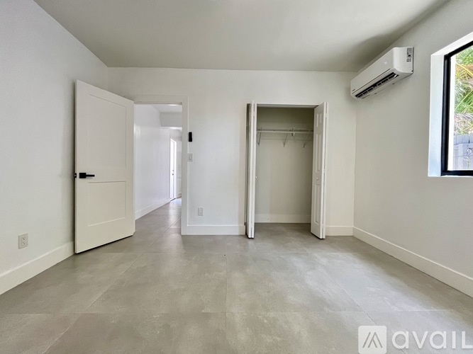 A spacious room with a door, a window, and a wall-mounted air conditioner unit.