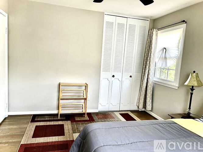 A bedroom with a bed, a window with curtains, a wooden chair, and a rug.