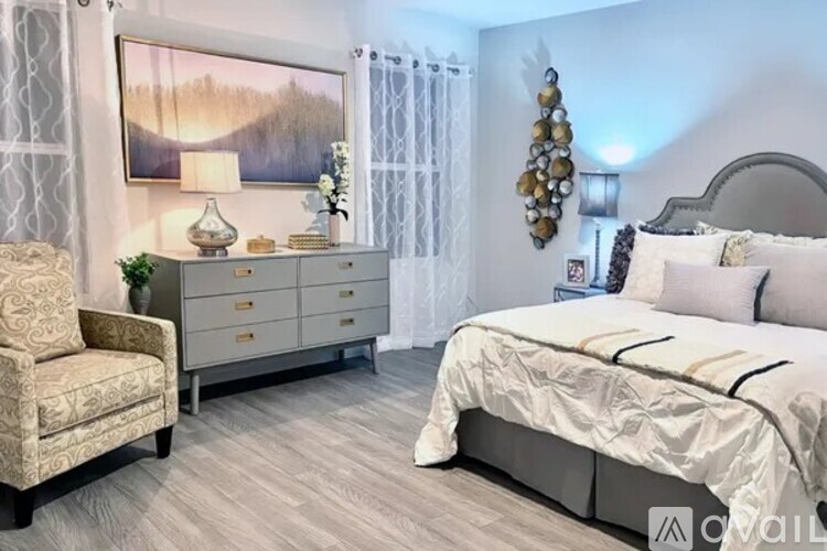 A bedroom with a large bed, a chair, and a dresser with a lamp on top.
