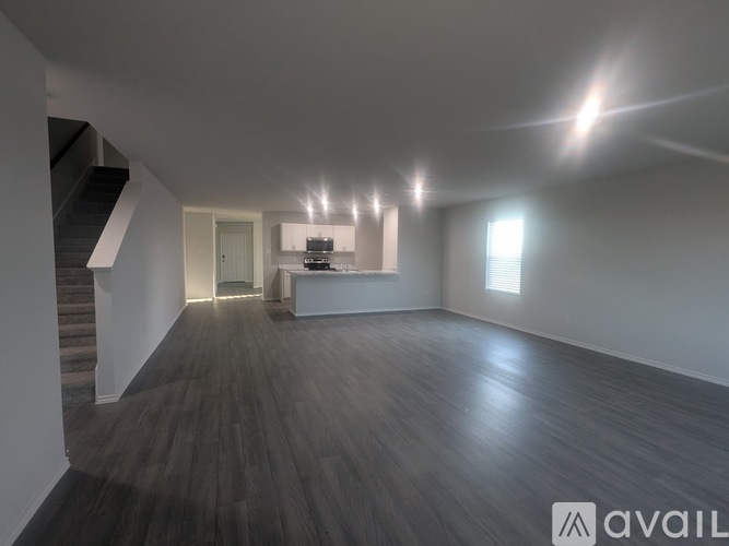 A spacious room with wooden flooring and a staircase on the left side.