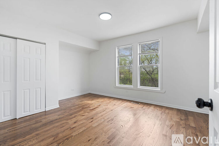 A room with wooden flooring and a window showing trees outside.