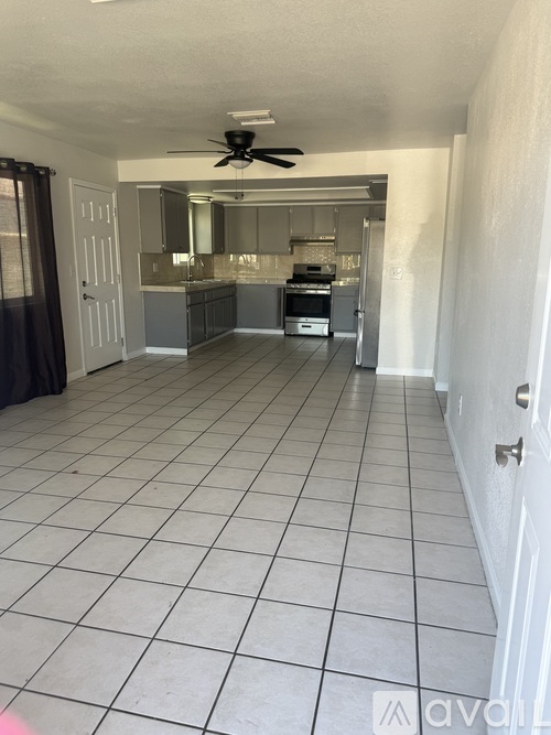 A spacious kitchen and living room with white tile flooring and a ceiling fan.