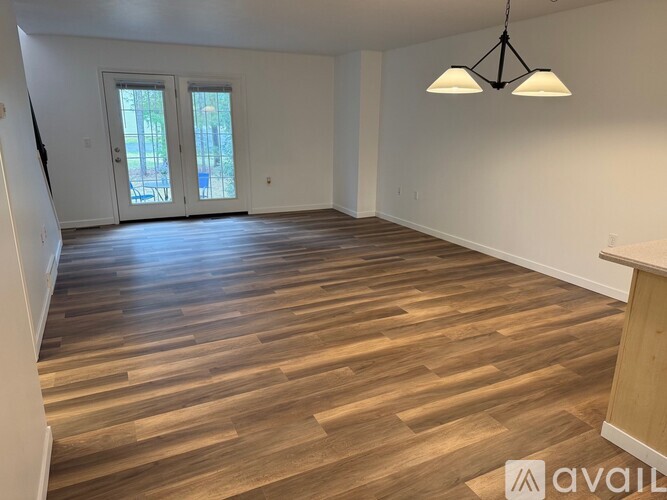 A room with wooden flooring and a large window with a view of trees.