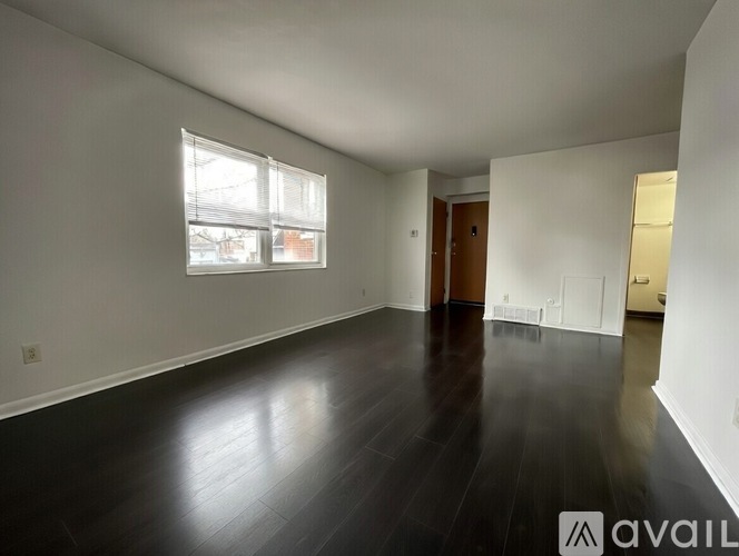 A spacious room with dark wood flooring and white walls.