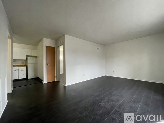 A spacious room with dark wood flooring and white walls.