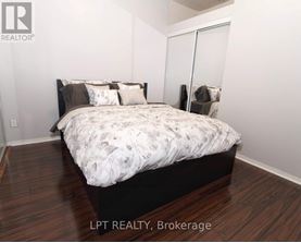 A bedroom with a bed, wooden floors, and a white wall.