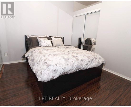 A bedroom with a bed, wooden floors, and a white wall.