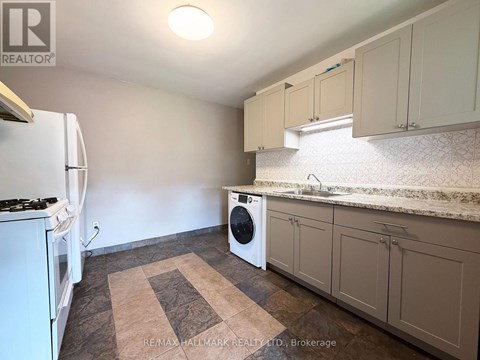 A kitchen with a white refrigerator, a washing machine, and a rug on the floor.