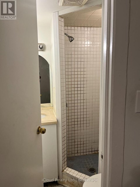 A white door with a gold handle is open to a bathroom with a tiled shower.