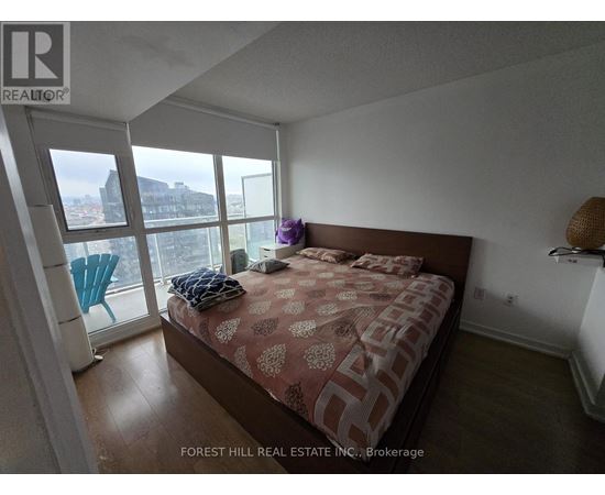 A bedroom with a bed, a chair, and a window overlooking a cityscape.