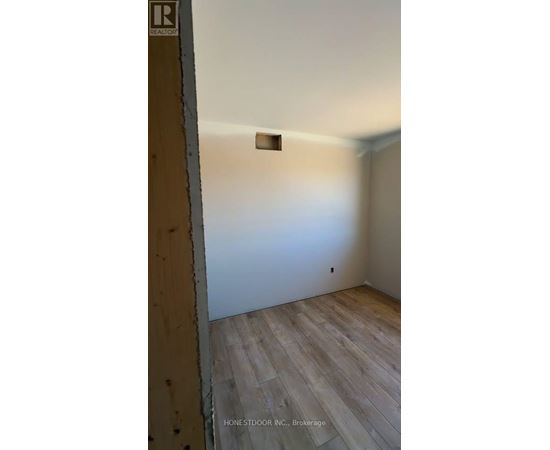 A room with wooden flooring and a white wall with a light switch.