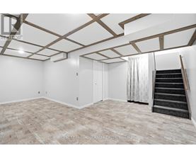 A spacious room with wooden beams on the ceiling and a staircase on the right side.