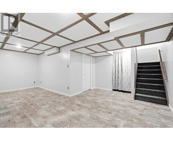 A spacious room with wooden beams on the ceiling and a staircase on the right side.