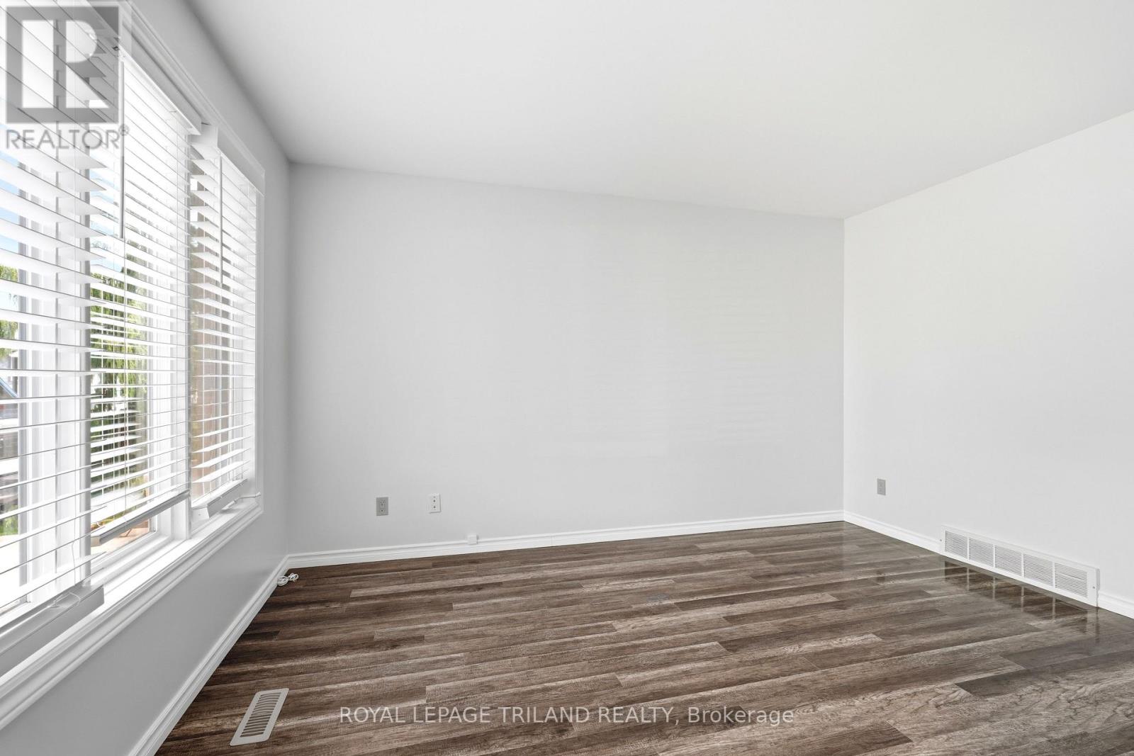 A room with wooden flooring and white walls, with a window on the left side.
