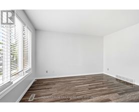A room with wooden flooring and white walls, with a window on the left side.
