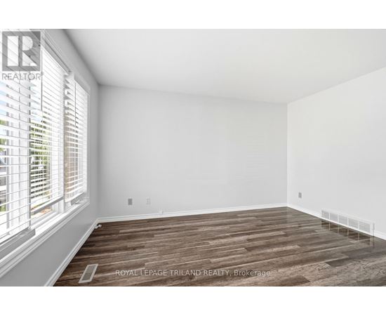 A room with wooden flooring and white walls, with a window on the left side.