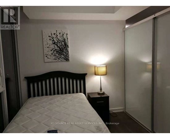 A bedroom with a white bed and a black and white painting on the wall.