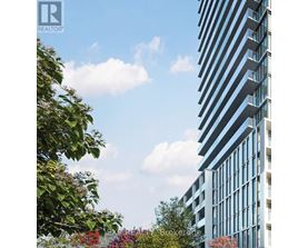 A tall building with many windows is surrounded by trees and bushes.