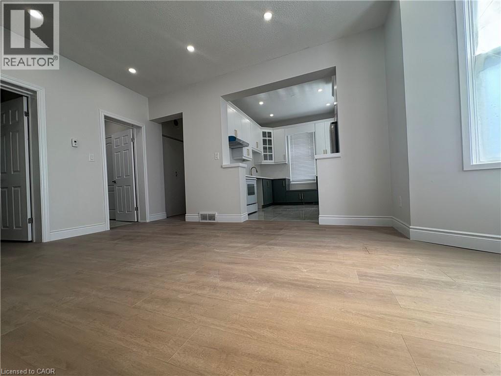 A spacious room with wooden flooring and a kitchen area in the background.