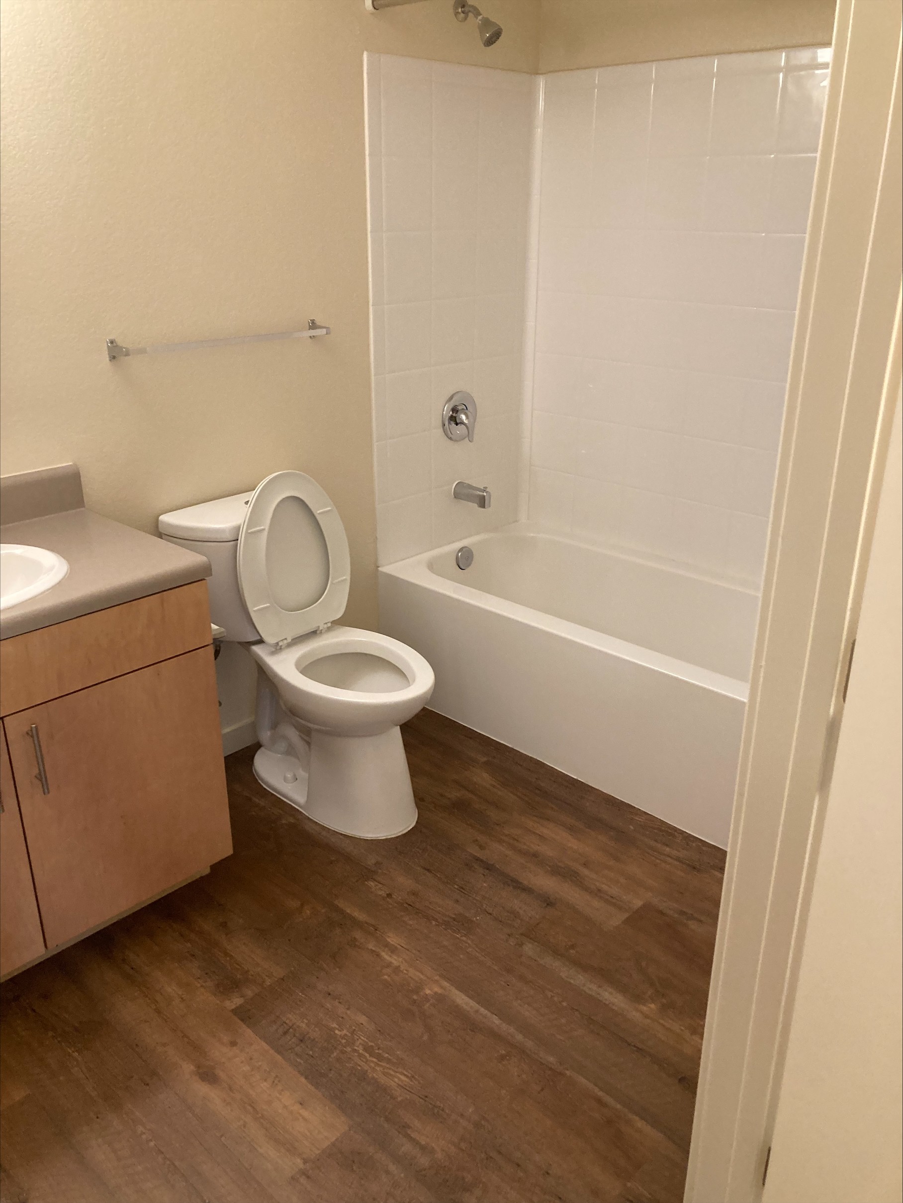 A white toilet sits in a bathroom with a wooden floor.