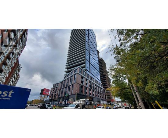 A tall building with a striped pattern is surrounded by trees and other buildings.