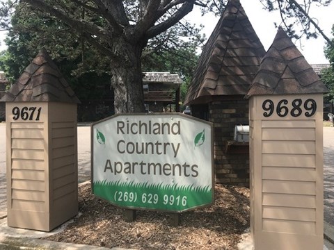 A sign for Richland Country Apartments is displayed in front of two small buildings.