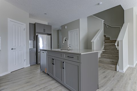 A kitchen with a refrigerator, cabinets, and a staircase.