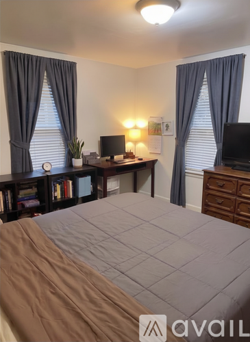 A bedroom with a bed, desk, and two windows with curtains.