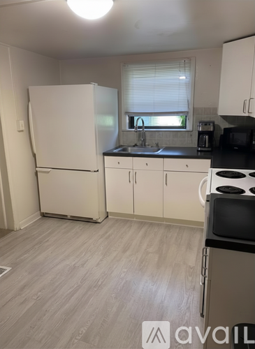 A kitchen with a white fridge, black countertops, and white cabinets.