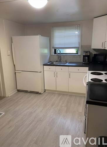 A kitchen with a white fridge, black countertops, and white cabinets.