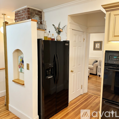 A black refrigerator in a kitchen with wooden floors and white walls.