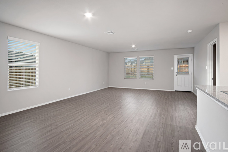 A spacious room with wooden flooring and a large window with blinds.