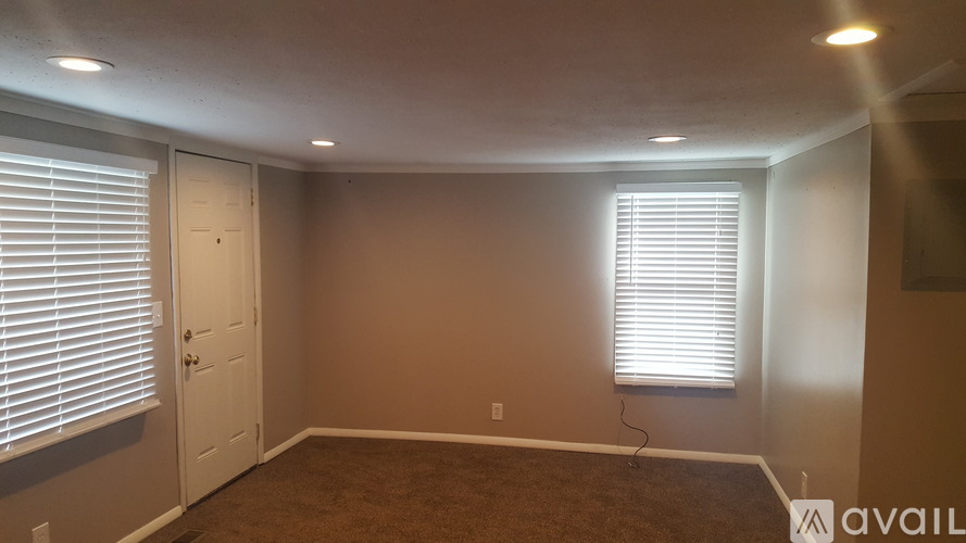A room with a carpeted floor, a door, and a window with blinds.