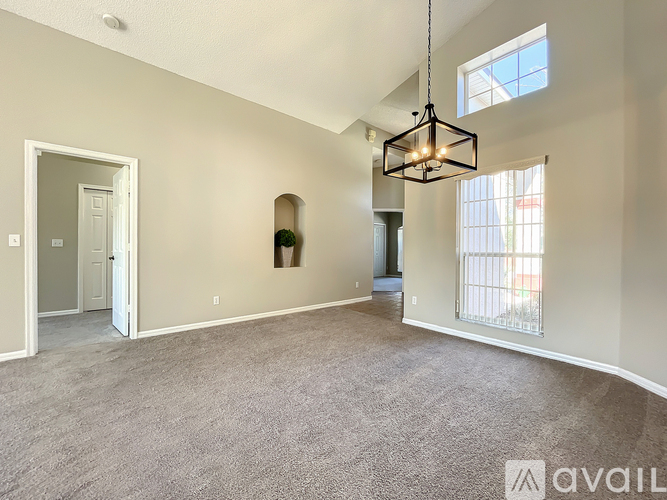 A spacious living room with a grey carpet and a hanging light fixture.