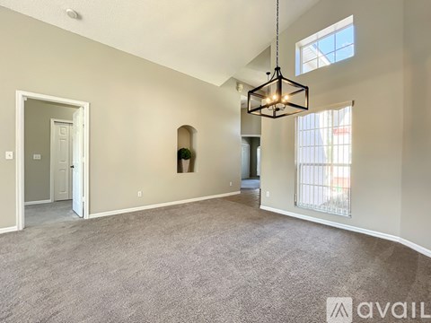 A spacious living room with a grey carpet and a hanging light fixture.