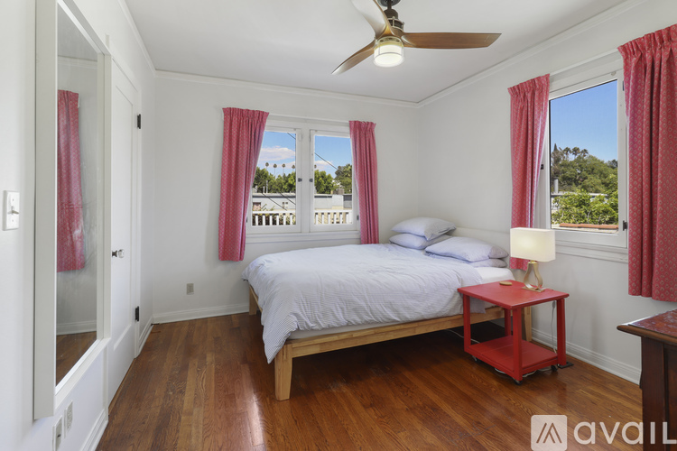 A bedroom with a bed, a ceiling fan, and a window with red curtains.