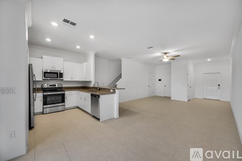 A spacious kitchen with white cabinets and appliances, a ceiling fan, and a tiled floor.