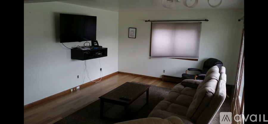 A living room with a brown couch and a flat screen TV mounted on the wall.