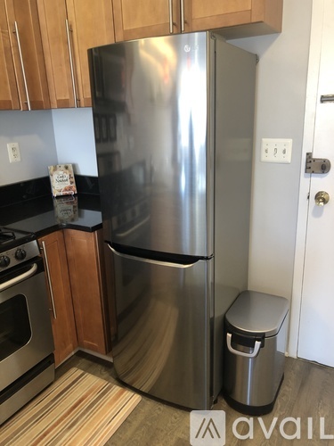 A stainless steel refrigerator stands in a kitchen next to a trash can.