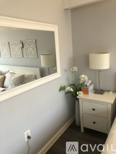 A bedroom with a bed, a nightstand with a lamp, and a mirror.