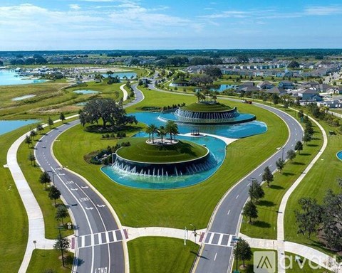 A beautiful aerial view of a roundabout with a fountain in the center, surrounded by a grassy area and roads.