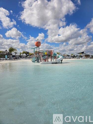 A playground with a slide and swings is in the foreground of a body of water.