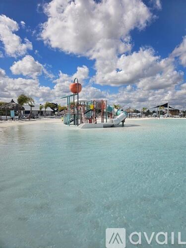 A playground with a slide and swings is in the foreground of a body of water.